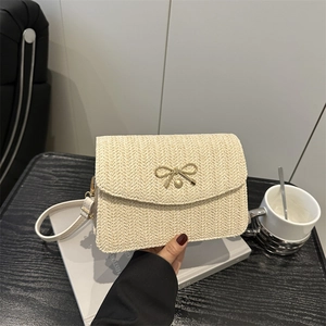 Gros plan du sac bandoulière en paille tressée crème avec nœud doré et bandoulière cuir