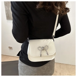 Close-up of white patent leather crossbody bag featuring a sparkling crystal butterfly bow
