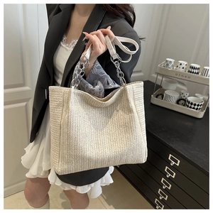 Close-up of woven straw tote bag featuring chain leather handles and silk scarf detail