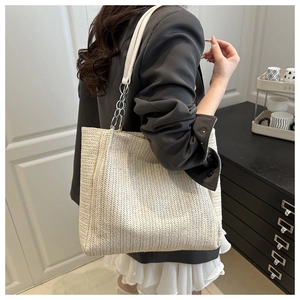 Close-up of woven straw tote bag with white leather straps and metal chain details