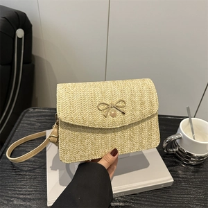 Détail du sac à bandoulière en paille tissée avec nœud doré et sangle en cuir beige