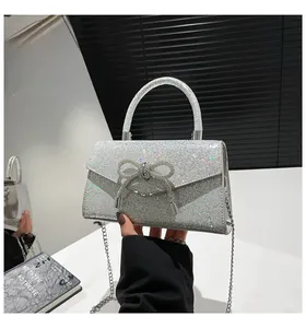 Detail of silver glitter evening bag featuring a sparkling rhinestone bow and chain strap