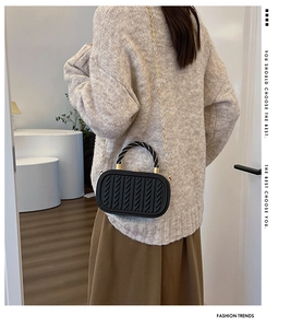 Detail of black woven texture handbag with gold chain and woven handle on model