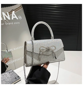 Close-up of shiny silver sequined handbag with crystal bow and thin metal chain strap