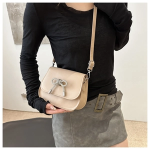 Detail view of cream crossbody bag with rhinestone butterfly bow worn by a model