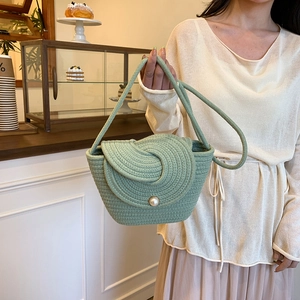 Sac seau tressé vert herbe avec boucle en perle porté par un mannequin en intérieur