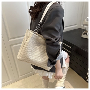 Close-up of woven straw tote bag with silver metal chain and white leather shoulder strap