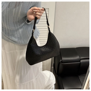 Detail of black faux leather baguette bag with animal texture and gold hardware on model