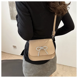 Beige crossbody bag with rhinestone butterfly detail shown on a female model