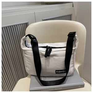 Détail d'un sac bandoulière en nylon blanc avec zips noirs et étiquette mode sur un livre