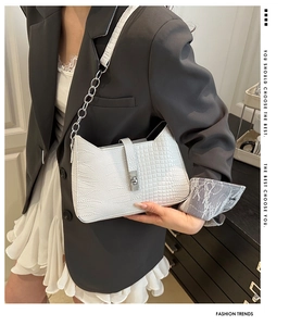 Detail of white crocodile embossed handbag with silver twist lock and chain strap on model