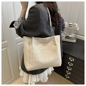 Detailed close-up of woven straw tote bag texture and white strap with silver metal links