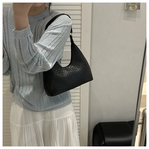 Close-up of black woven leather shoulder bag with gold hardware worn by a model