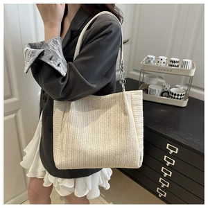 Detail of a woven tote bag with herringbone texture and metallic chain shoulder strap