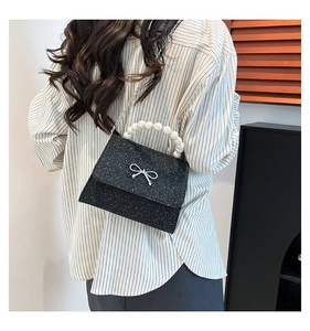 Detail of black glitter handbag with pearl handle and silver bow on its flap