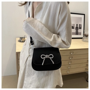 Detailed shot of a black flap crossbody bag featuring a silver rhinestone butterfly bow buckle