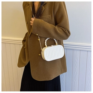 Detail of white cable-knit texture on a structured crossbody bag with gold chain strap