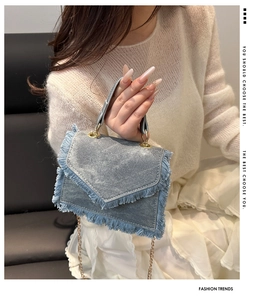 Detail der hellblauen Denim-Handtasche mit langen Fransen und goldenen Ringgriffen
