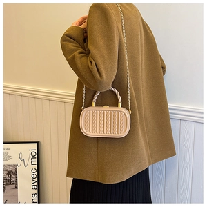 Side view of beige embossed box bag with gold chain strap and twisted handle on model