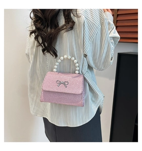 Pink glitter handbag featuring pearl handle and metal bow detail shown on a person