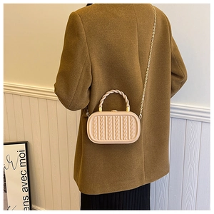 Detail of beige oval handbag with textured vertical weave and gold chain strap