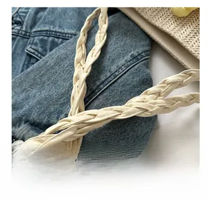Detailed macro view of woven cream shoulder strap and texture on straw tote bag
