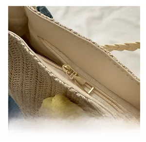 Detailed close-up of the smooth golden metal zipper closure on a beige woven straw tote bag
