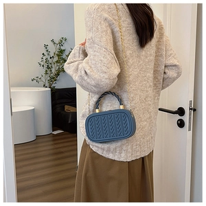 Detail of blue embossed mini box bag featuring gold chain and woven handle on a model