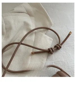 Detail of a brown leather shoulder bag handle featuring a dual knot design and gold metal tips
