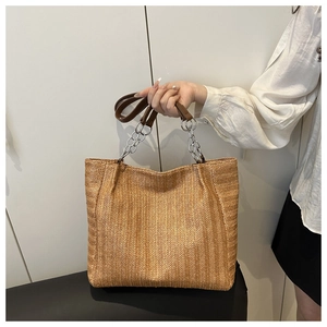 Detailed view of woven straw tote bag featuring silver chain and brown leather handles