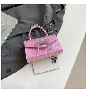 Pink sequin evening bag with crystal bow detail shown next to a smartphone for size