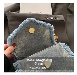 Detailansicht der hellblauen Denim-Umschlagtasche mit Fransen und Gold-Magnetverschluss