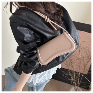 Detail of beige saddle bag with knotted strap and gold logo on a stylish model