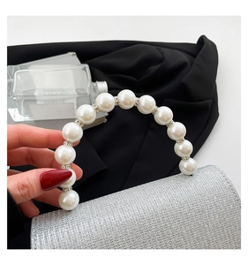 Detail of silver sequin handbag featuring a white pearl handle and rhinestone accents