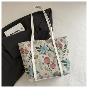 Close-up of floral embroidery on a beige woven tote bag with white leather straps