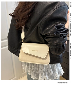 Detail of cream crossbody bag with woven texture, wide geometric strap and gold lettering
