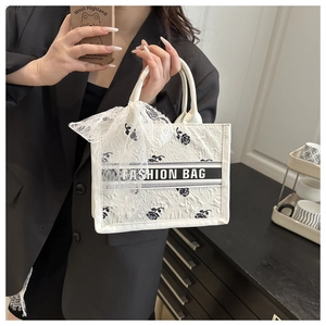 Detail of white textured tote bag with black rose patterns and lace bow accessory