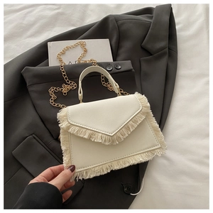 Détail du sac à main crème à franges avec chaîne dorée sur un blazer gris chic