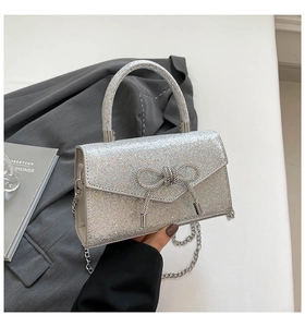 Detail of silver glitter evening bag with rhinestone bow and metallic chain strap