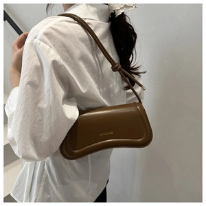 Detail of dark brown leather shoulder bag with gold logo and knotted strap on white shirt