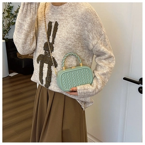 Detail of mint green embossed box bag featuring a knotted handle and gold chain strap