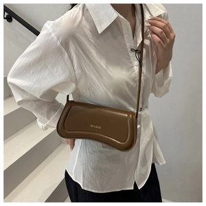 Detail of a wave-shaped brown leather crossbody bag with XM & BAGS gold logo branding