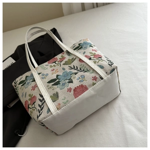 Close-up of floral embroidery on off-white canvas tote bag with white leather straps