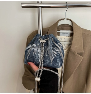 Close-up of denim bucket bag with silver sequins, chain strap and pearl drawstring detail
