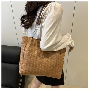 Detailed view of woven straw tote bag with brown leather and silver chain strap