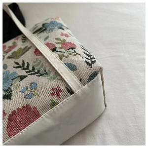 Detailed view of floral jacquard fabric and white PU leather stitching on a tote bag