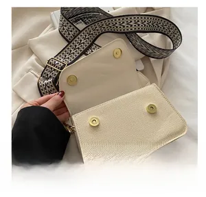 Detail showing the magnetic gold metal buckle and woven texture of the beige crossbody bag