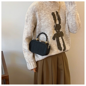 Detail shot of black woven embossed texture and two-tone rope handle on chic chain handbag