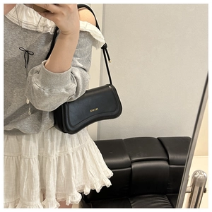 Minimalist black crescent shoulder bag with gold logo shown in a lifestyle mirror selfie