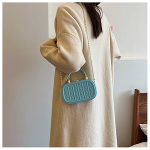 Detail of light blue crossbody bag with embossed texture and gold chain strap worn by a person